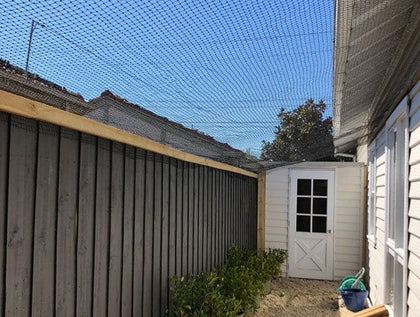 A cat-netted side alley between a house and a fence